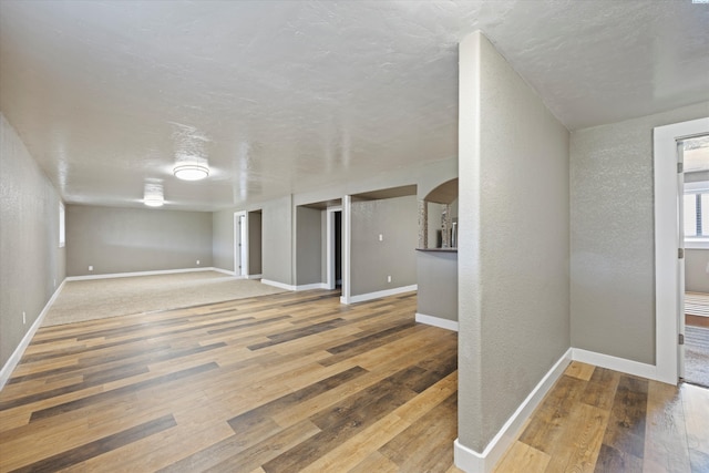 interior space with arched walkways, baseboards, a textured wall, and hardwood / wood-style floors