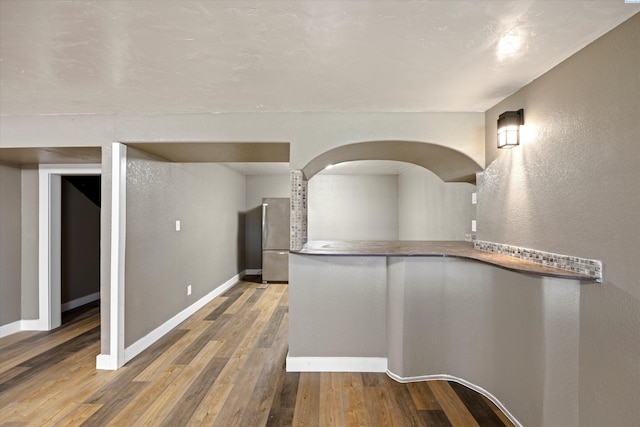 hallway featuring baseboards, arched walkways, wood finished floors, and a textured wall