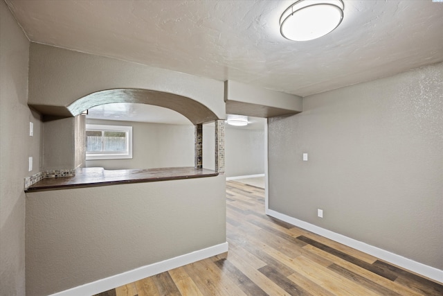 kitchen featuring arched walkways, a textured wall, baseboards, and wood finished floors