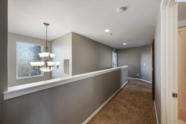 corridor with a textured ceiling, carpet floors, visible vents, baseboards, and an inviting chandelier