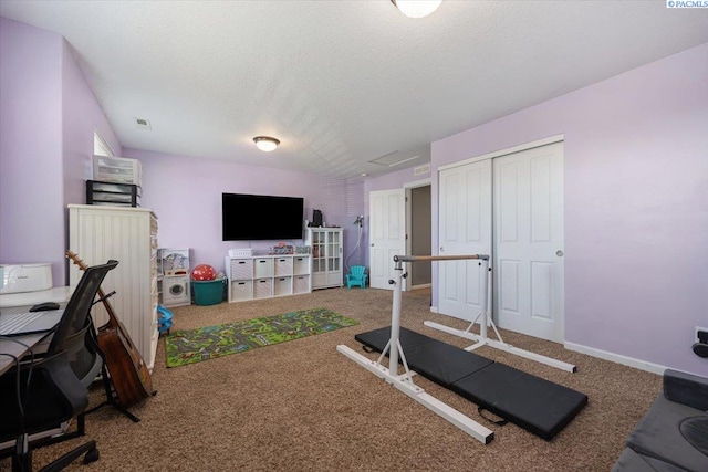 exercise area with visible vents, attic access, carpet flooring, a textured ceiling, and baseboards