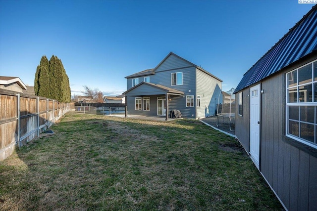 back of property with a patio, a trampoline, a fenced backyard, and a lawn