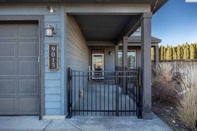 view of exterior entry with covered porch, a gate, and fence