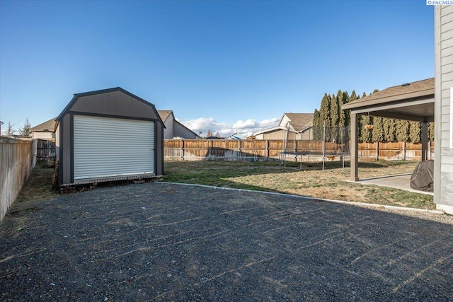 view of yard with a trampoline, an outbuilding, a fenced backyard, and a storage unit