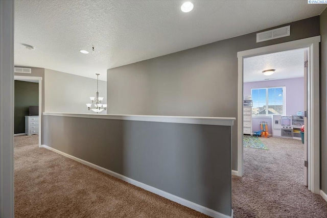 hall featuring carpet floors, baseboards, visible vents, and a textured ceiling