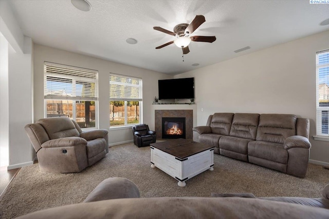 carpeted living area with a ceiling fan, baseboards, visible vents, and a tiled fireplace