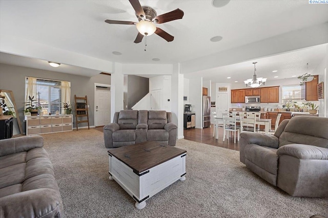 carpeted living room featuring ceiling fan with notable chandelier