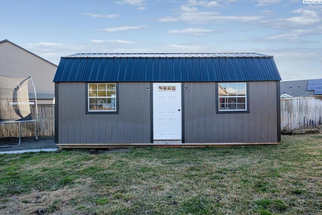 view of outbuilding featuring a trampoline, a fenced backyard, and an outdoor structure