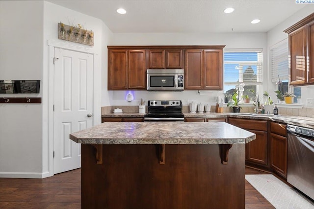 kitchen with appliances with stainless steel finishes, dark wood-style flooring, a sink, and a kitchen island