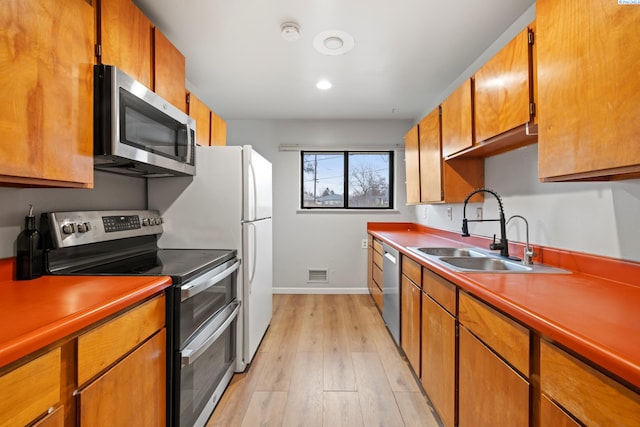 kitchen featuring light wood finished floors, visible vents, appliances with stainless steel finishes, brown cabinets, and a sink