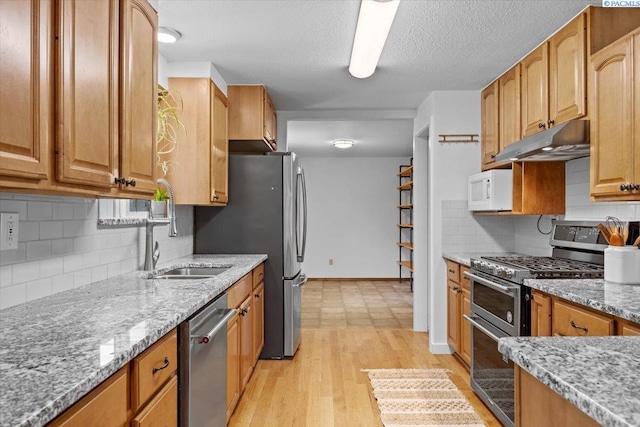 7009 W 8th Ave, Kennewick, WA 99336 - kitchen featuring appliances with stainless steel finishes, under cabinet range hood, decorative backsplash, light stone counters, and light wood-style floors