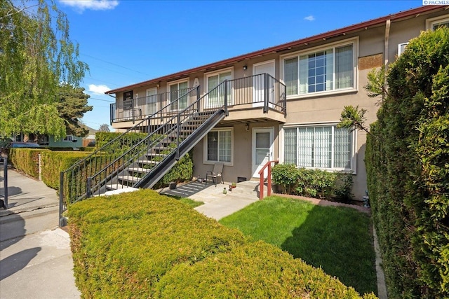 view of front of house with stucco siding, a balcony, stairs, and a front yard