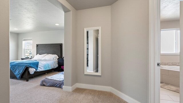 bedroom featuring ensuite bathroom, baseboards, carpet, and a textured ceiling