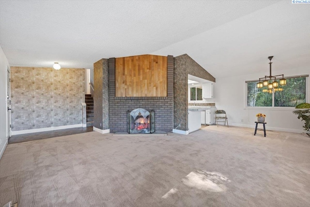 unfurnished living room with a fireplace, lofted ceiling, carpet floors, a textured ceiling, and an inviting chandelier