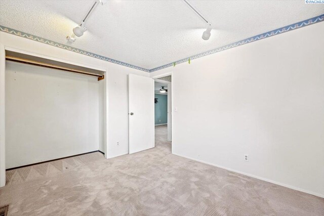 unfurnished bedroom featuring rail lighting, light carpet, a textured ceiling, and a closet