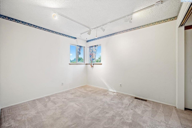 spare room featuring light colored carpet, rail lighting, and a textured ceiling