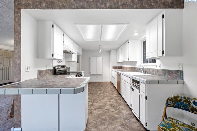 kitchen with stainless steel appliances, tile countertops, kitchen peninsula, and white cabinets