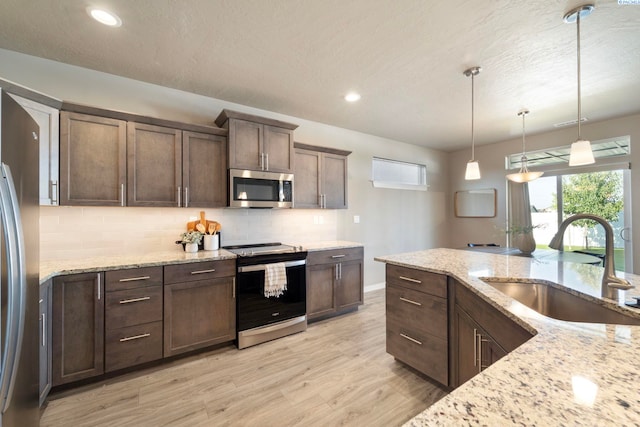 6223 Berea Ln, Pasco, WA 99301 - kitchen with stainless steel appliances, decorative backsplash, light wood-style floors, dark brown cabinetry, and decorative light fixtures