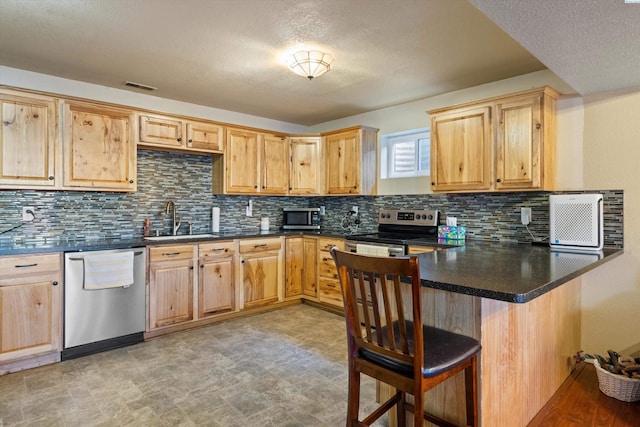 kitchen with sink, a breakfast bar area, appliances with stainless steel finishes, kitchen peninsula, and backsplash