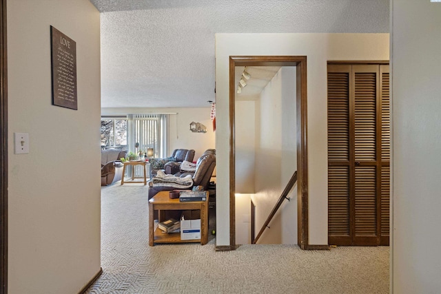 hallway with light colored carpet and a textured ceiling