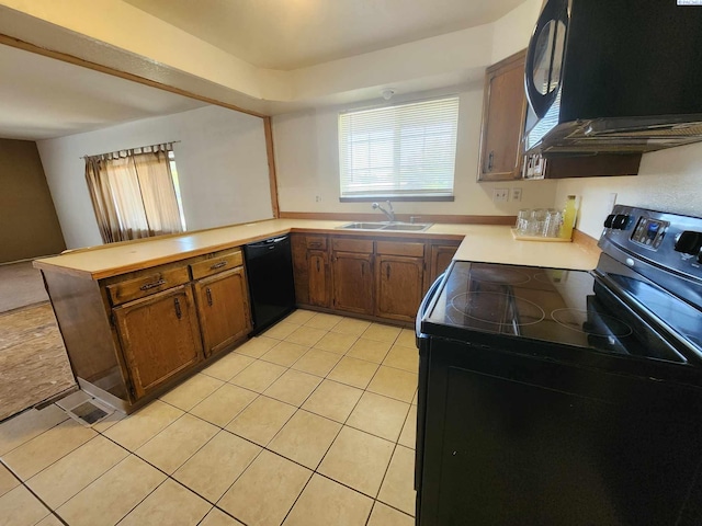 kitchen featuring a peninsula, light tile patterned flooring, light countertops, a sink, and black appliances