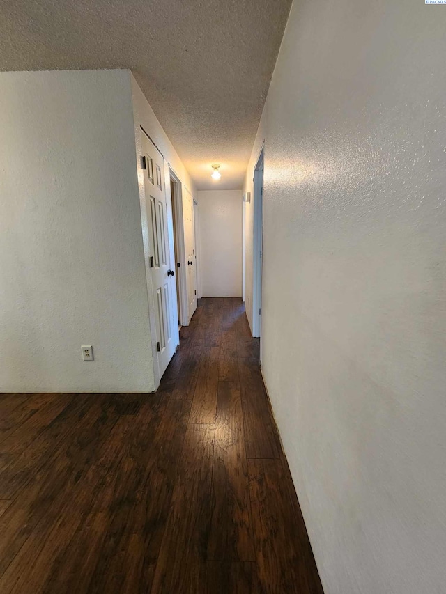 hall with a textured ceiling and dark wood-type flooring