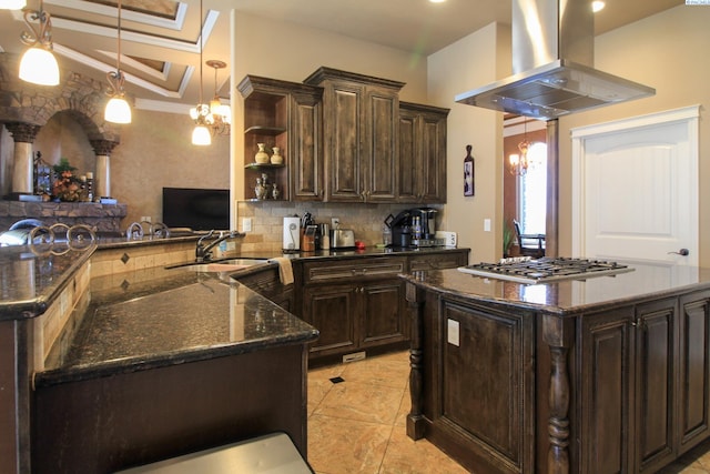 kitchen with dark brown cabinetry, stainless steel gas cooktop, kitchen peninsula, pendant lighting, and island exhaust hood