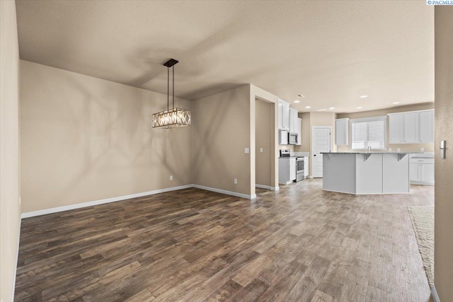 unfurnished living room with baseboards, recessed lighting, wood finished floors, and a chandelier