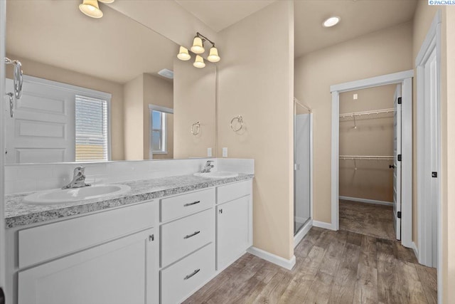 full bath with a sink, double vanity, a stall shower, and wood finished floors