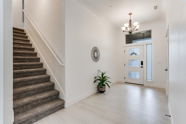 foyer entrance with ornamental molding, light wood-type flooring, and an inviting chandelier