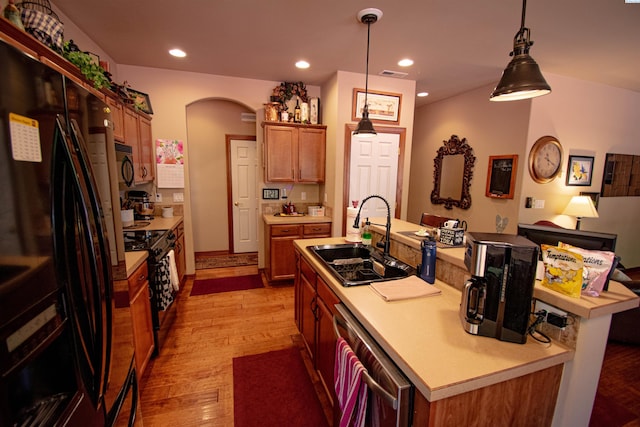 kitchen with a center island with sink, visible vents, light wood-style flooring, a sink, and black appliances