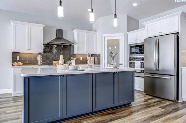 kitchen featuring wall chimney range hood, decorative backsplash, light countertops, stainless steel appliances, and white cabinetry
