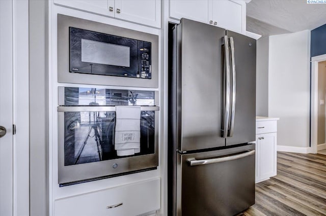 kitchen featuring freestanding refrigerator, white cabinets, baseboards, and light wood-type flooring