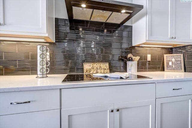 kitchen with wall chimney range hood, tasteful backsplash, light stone counters, white cabinets, and black electric stovetop