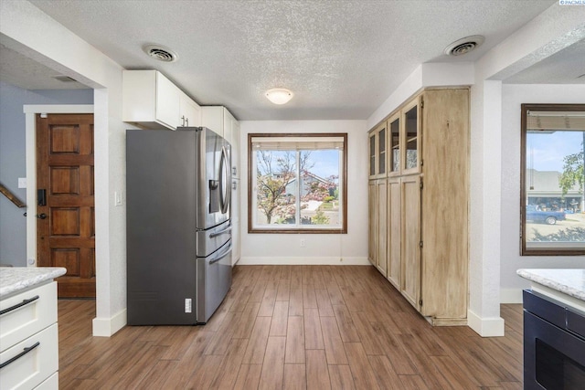 kitchen with a textured ceiling, baseboards, visible vents, and stainless steel fridge