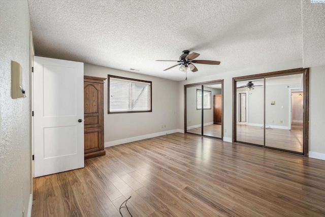 unfurnished bedroom with visible vents, multiple closets, wood finished floors, a textured ceiling, and a ceiling fan