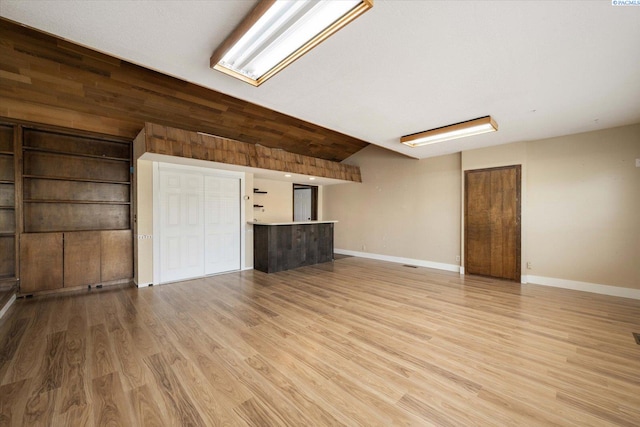 unfurnished living room with baseboards, vaulted ceiling, and light wood-type flooring