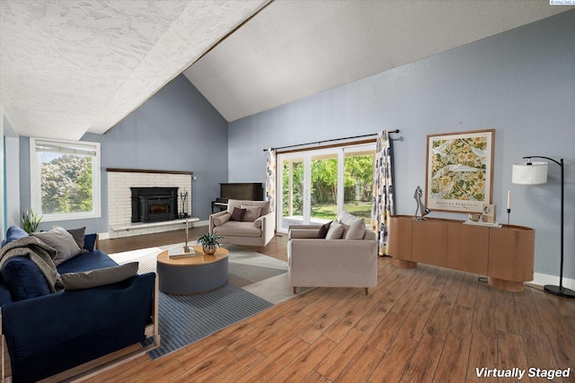 living area with wood finished floors, a fireplace, a healthy amount of sunlight, and high vaulted ceiling