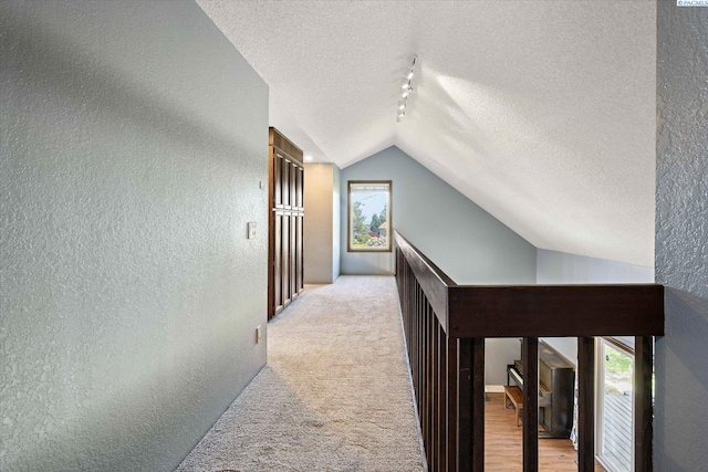 corridor featuring a textured ceiling, a textured wall, vaulted ceiling, and rail lighting