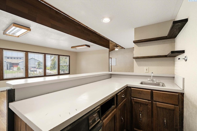 kitchen with open shelves, dark brown cabinetry, a sink, light countertops, and a peninsula