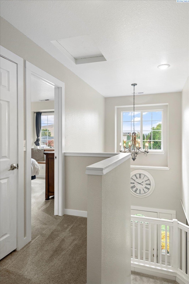 corridor featuring a notable chandelier, a textured ceiling, an upstairs landing, and light colored carpet