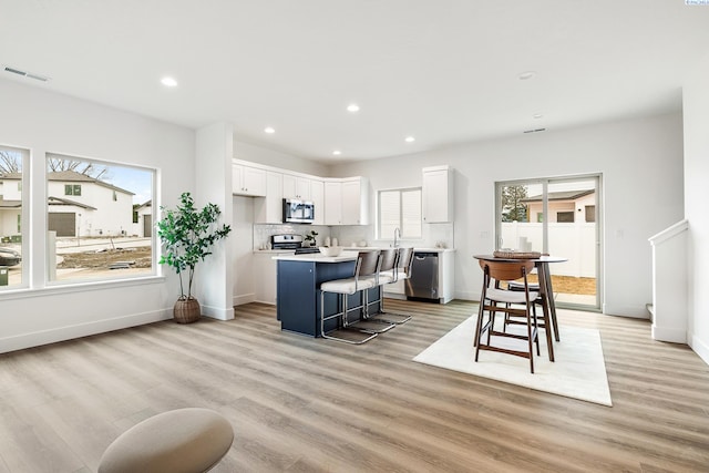 kitchen featuring a kitchen breakfast bar, a center island, light wood-type flooring, white cabinets, and stainless steel appliances
