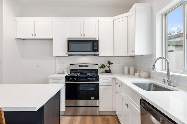 kitchen with a sink, appliances with stainless steel finishes, white cabinets, and light stone countertops
