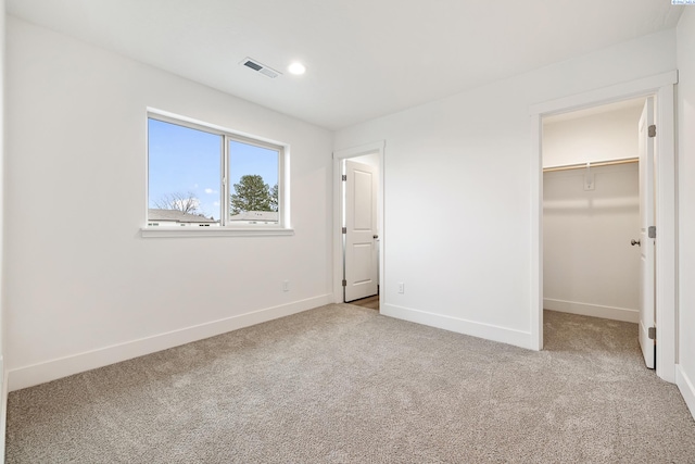 unfurnished bedroom featuring carpet flooring, a walk in closet, recessed lighting, baseboards, and visible vents