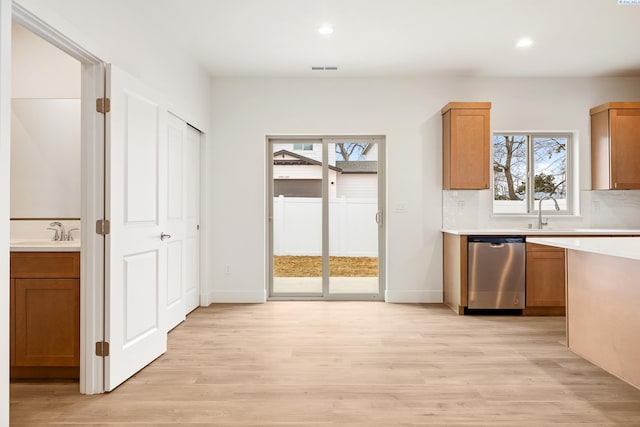kitchen featuring light countertops, stainless steel dishwasher, light wood-type flooring, and a healthy amount of sunlight