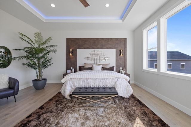 bedroom featuring a raised ceiling, ceiling fan, and light wood-type flooring