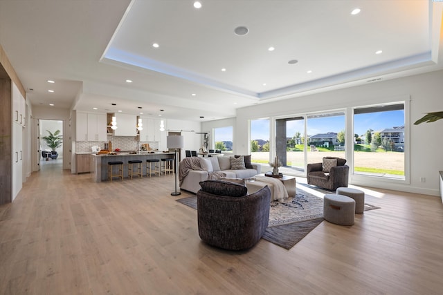 living room with a raised ceiling and light wood-type flooring