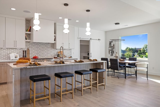 kitchen with a barn door, light stone countertops, an island with sink, and white cabinets