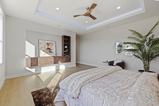 bedroom with a raised ceiling, ceiling fan, and light wood-type flooring