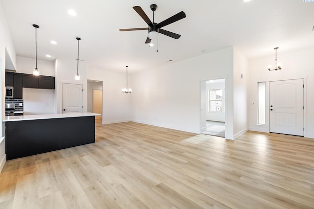 unfurnished living room featuring ceiling fan with notable chandelier, light wood finished floors, recessed lighting, and baseboards